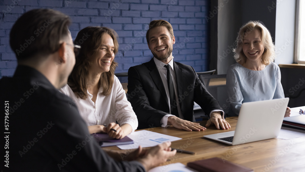 Cheerful business colleagues meeting at table for work discussion, talking, laughing, brainstorming, having fun. Happy confident male boss talking to diverse employees on briefing Cheerful business colleagues meeting at table for work discussion, talking, laughing, brainstorming, having fun. Happy confident male boss talking to diverse employees on briefing