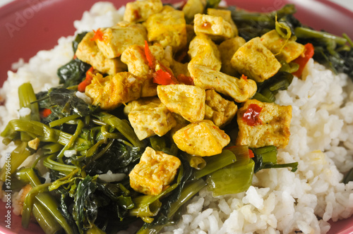 stir-fried water spinach with sliced tofu and white rice served on a red plastic plate with a napkin photo