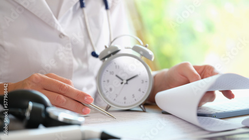 Doctor with alarm clock and documents on hospital table.