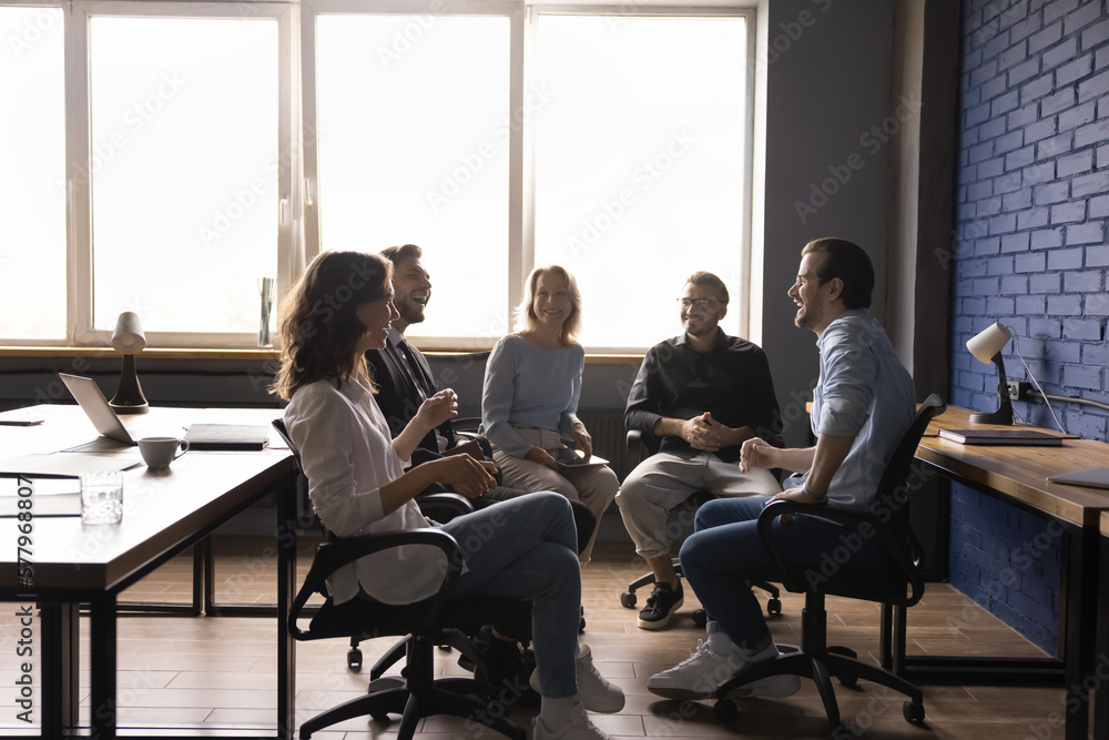 Cheerful diverse team sitting on chairs in circle, brainstorming on project, discussing ideas, strategy, plan, smiling, laughing. Group of addicts meeting for support therapy