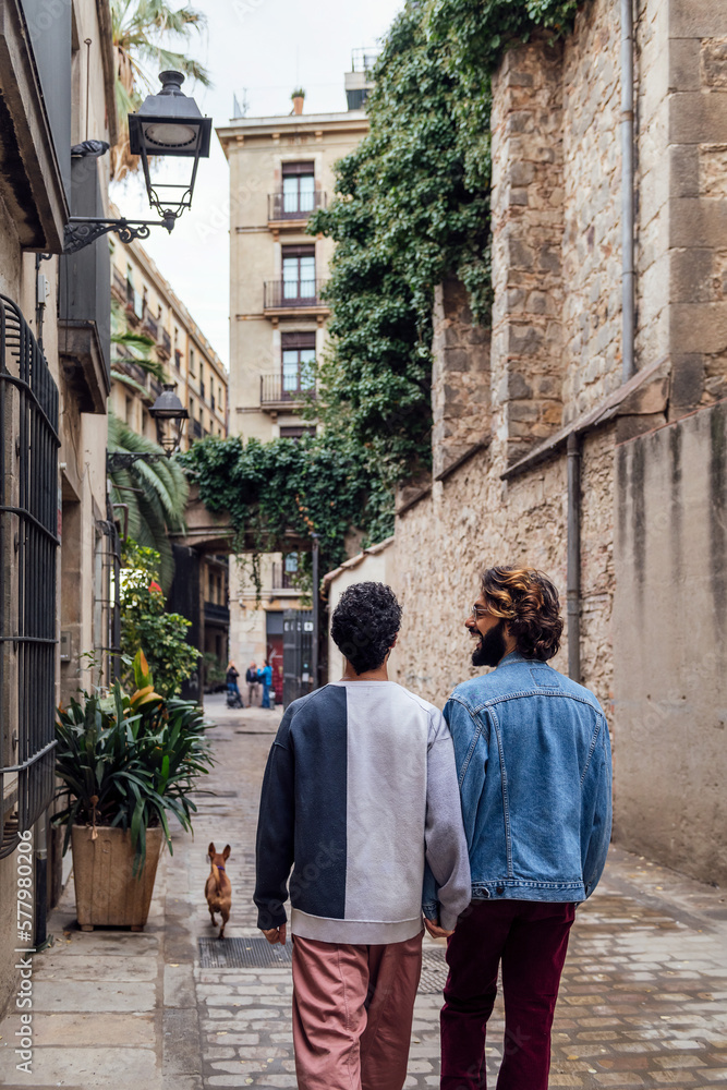 rear view of a gay male couple strolling happy down a cobbled street holding hands, concept of leisure and love between people of the same sex, copy space for text