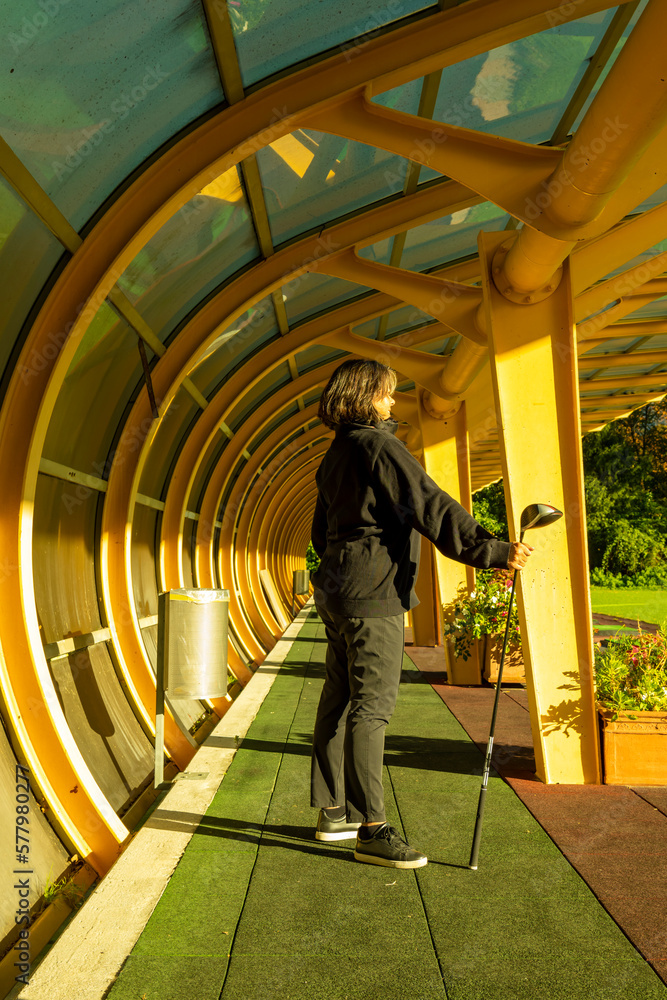 Golfer Standing and Holding Her Golf Club Driver in a Built Structure on Driving Range on Golf Course in a Sunny Day in Switzerland. Golfer Standing and Holding Her Golf Club Driver in a Built Structure on Driving Range on Golf Course in a Sunny Day in Switzerland.