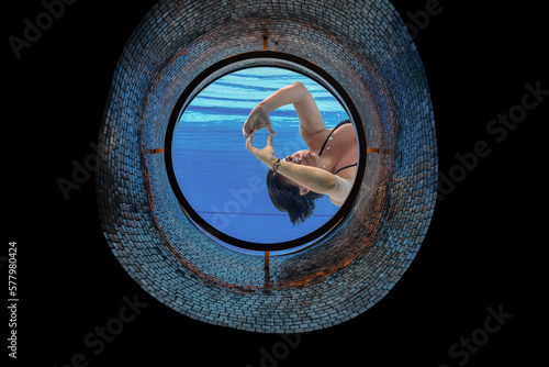 Woman Making a Heart Shape with Her Hands in the Ship Porthole in Underwater in Swimming Pool in a Sunny Day in Switzerland.