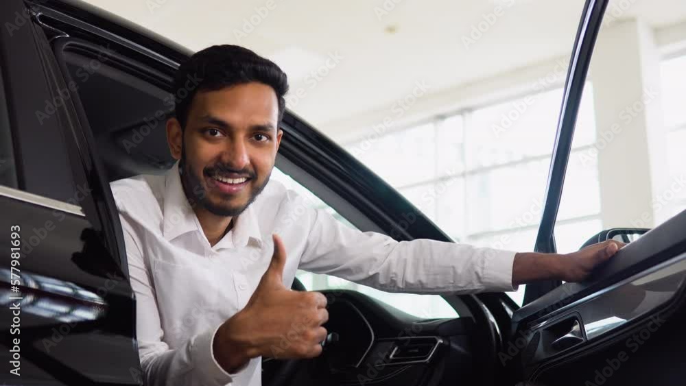 Happy successful indian man sitting in his new electric car in auto showroom. The buyer selects a car Happy successful indian man sitting in his new electric car in auto showroom. The buyer selects a car