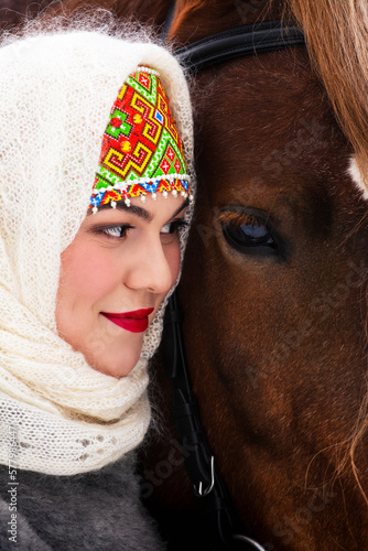 Obraz na płótnie Сlose portrait of a Russian beauty girl in traditional clothes with red big horse in forest winter. w salonie