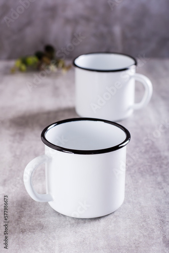 Two white empty metal mugs on a gray background in a vertical view
