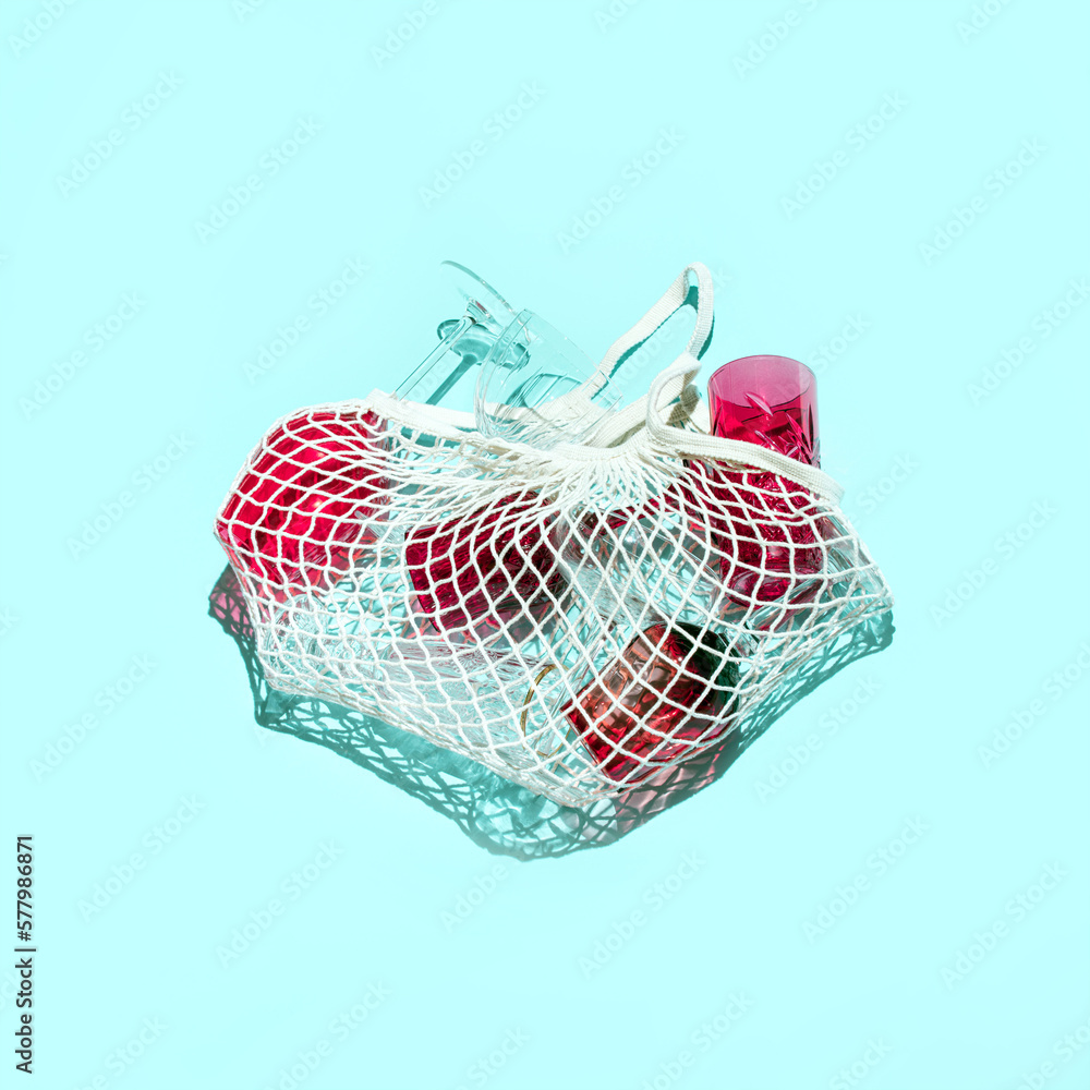Fototapeta premium Various drinking glasses in a mash grocery bag, creative party concept, pastel blue background. 