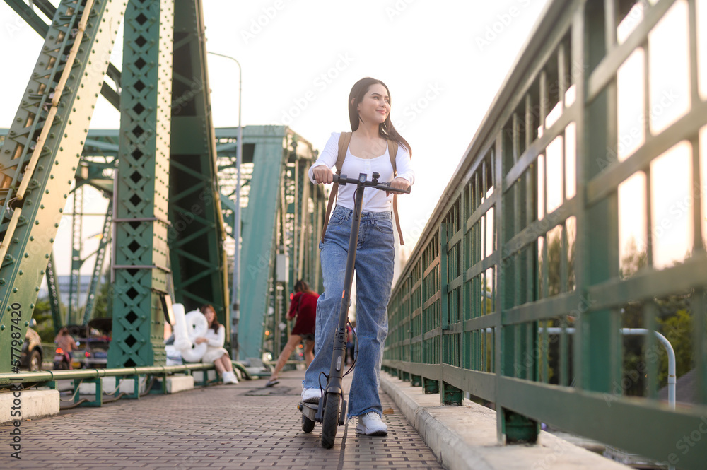 Portrait of young beautiful woman with an electric scooter  over bridge in modern city  background