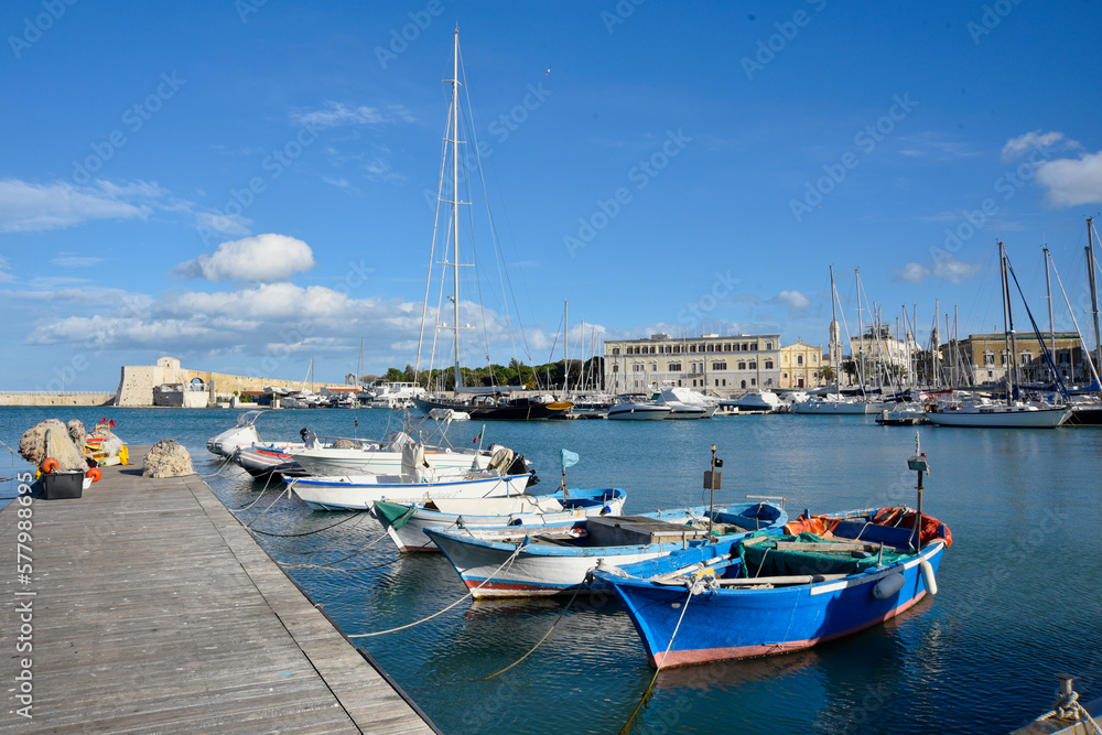Fishing boats docked at the piers in Trani, Italy. View of historical buildings, turquoise water and clear sky