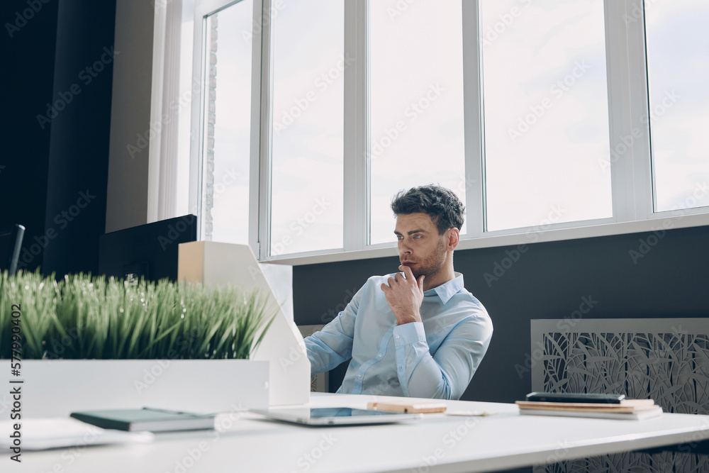 Handsome young businessman using computer while sitting at his working place in office Handsome young businessman using computer while sitting at his working place in office