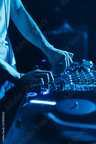 Club DJ mixing vinyl records in blue stage lights. Disc jockey playing music on party in night club