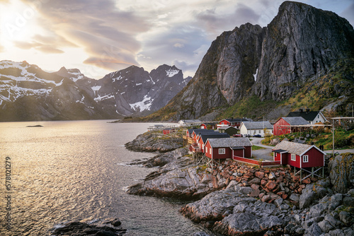 Typical red houses in Reine, Lofoten, Norway, overlooking the lake and the mountain during a clear spring day with clouds