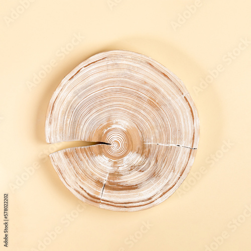 Round with crack brushed and painted in white color wooden cross slice of larch tree on light yellow photo