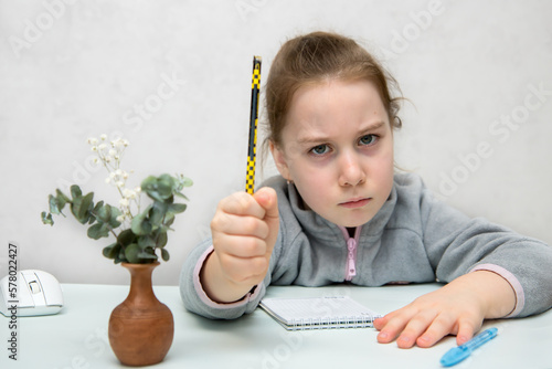 Billede på lærred frowning girl sits at a table holding a pencil in her fist and threatening someo