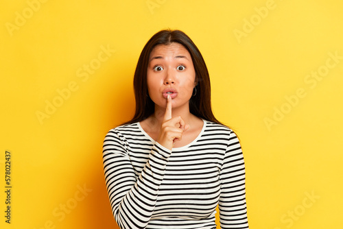 Fotografie Photo of trendy caucasian brunette woman in striped t-shirt presses index finger