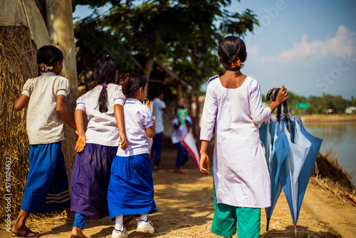 Taherpur, Bangladesh – November 05, 2019: Back view of school children rushing to attend the school in a remote village. Girls education, a group of teenage girls going to the school together.