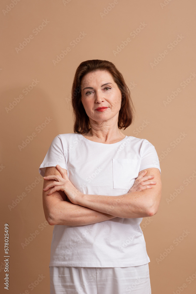 A beautiful an aged woman with a beautiful figure, her face is covered with wrinkles. Standing on a beige background and smiling
