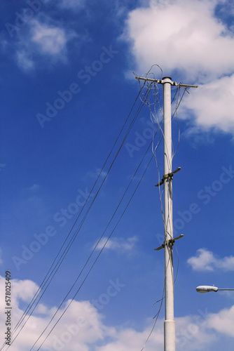 Bottom view of utility poles with blue sky. Blue sky and white clouds. Illustration on the theme of electricity supply. Rural electrification.