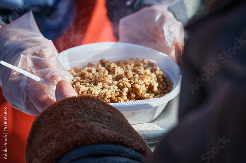 Wallpaper Mural A volunteer passes a plate of food to a starving man on the street. The concept of poverty and hunger. Groats of hot buckwheat porridge. Sunny cold day. Selective focus. Torontodigital.ca
