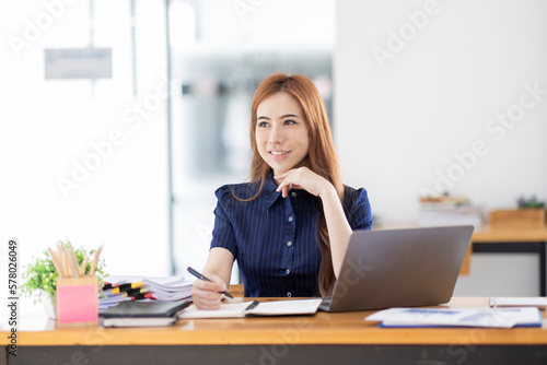 Asian Businesswoman Using laptop computer and working at office with calculator document on desk, doing planning analyzing the financial report, business plan investment, finance analysis concept. 