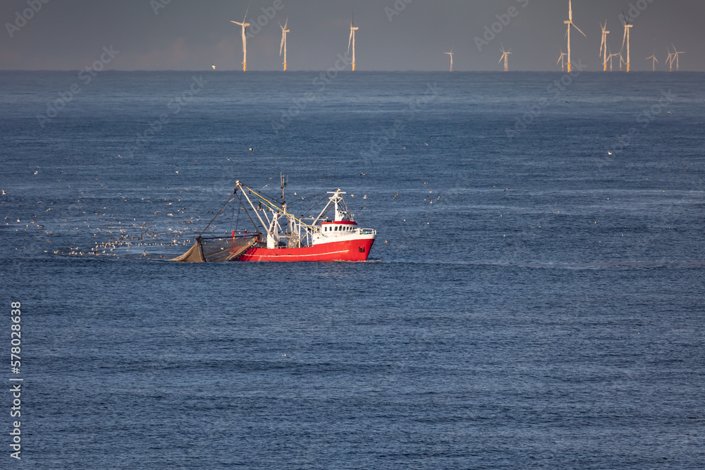 Obraz premium A cutter with lifted drag nets on the North sea with wind turbines in the background