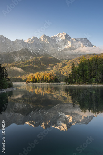 Spiegelung von Bergen mit Wolken im morgendlichen Licht in See. Zugspitze und Eibsee in Bayern.
