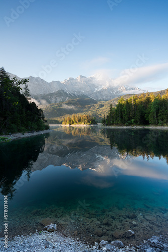 Fototapeta Naklejka Na Ścianę i Meble -  Spiegelung von Bergen mit Wolken im morgendlichen Licht in See. Zugspitze und Eibsee in Bayern.