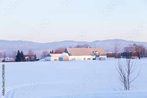 Early morning pastel winter view of metal roofed white barns in snowy field, with the Laurentian mountains in the background, St. Pierre, Island of Orleans, Quebec, Canada