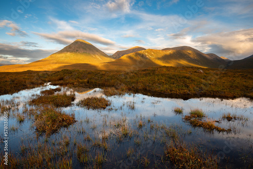 Red Cuillins covered in golden light seen from boggy moorland near Sligachan. Isle of Skye, Scotland, UK.