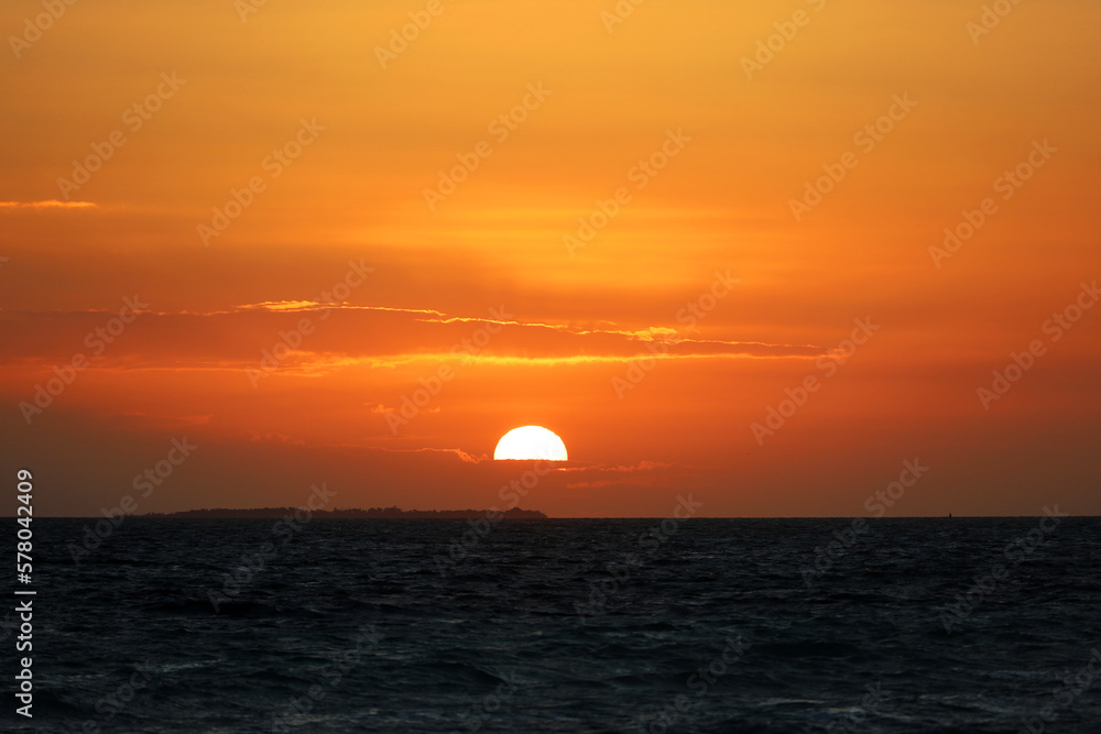 Sunrise on a beach, orange sun is shining through the clouds and reflected in dark waves. Morning sea background for romantic travel