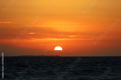 Sunrise on a beach  orange sun is shining through the clouds and reflected in dark waves. Morning sea background for romantic travel