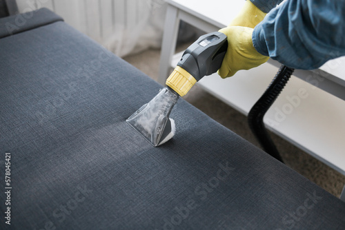 Foto Man in protective rubber glove cleaning sofa with professionally extraction method with washing vacuum cleaner