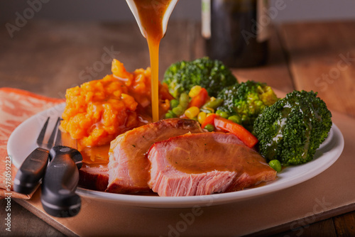 Gammon roast dinner with gravy being poured over it in a rustic setting. photo