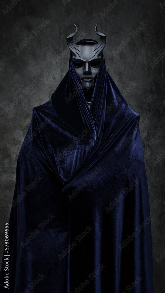 Studio shot of follower of dark cult dressed in dark robe and horned mask.