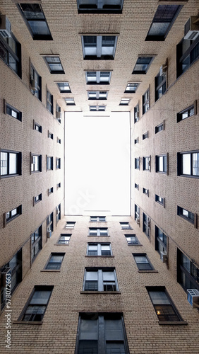 Light at the end of the tunnel. Abstract upwards view of New York City building courtyard opening to overexposed sky. Wide angle, 16:9 aspect ratio, vertical orientation