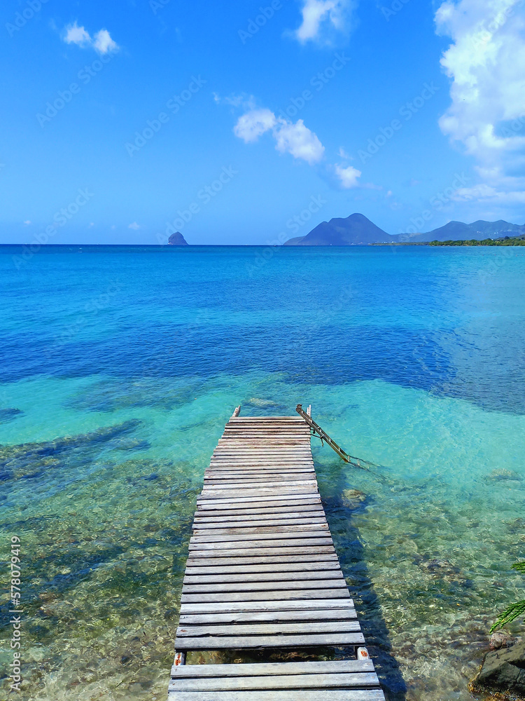 Pier at beach in Landscape of the French West Indies. The wooden bridge stretches into the sea. Beautiful tropical with Mountain clouds and sky.
