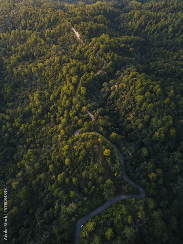 Aerial view of countryside road passing through the green forrest and mountain
