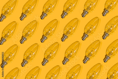 Yellow background. Electric light bulbs pattern. An old glass electric light bulb with a tungsten filament. The concept of electricity consumption and saving. Obsolete energy.