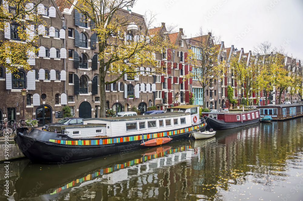 View over a wide canal in Amsterdam with houseboats at dock and houses in the background.