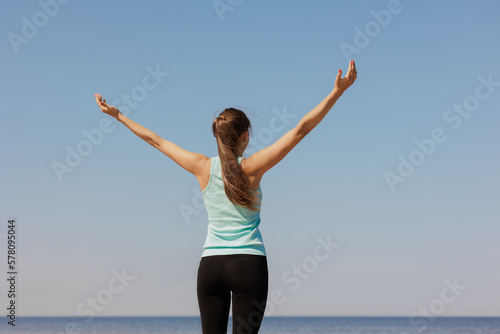yoga and freedom, sporty woman does warm-up on seashore in morning with hands to sides. fitness millennial female trains, asana breathing practice, healthy lifestyle, love for your body, mental and
