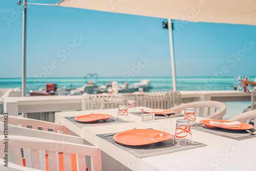 Relaxing outdoor restaurant at the beach. Table setting at tropical beach restaurant. Elegant white wooden tables, chairs under beautiful soft sunset sky, sea view. Luxury hotel or resort restaurant © icemanphotos