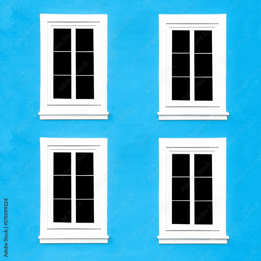 PVC Windows. Architecture background. Vibrant color blue wall facade. Small town house exterior. Street of European city building. Four window frames isolated on empty wall. Simple windows in a row. PVC Windows. Architecture background. Vibrant color blue wall facade. Small town house exterior. Street of European city building. Four window frames isolated on empty wall. Simple windows in a row.