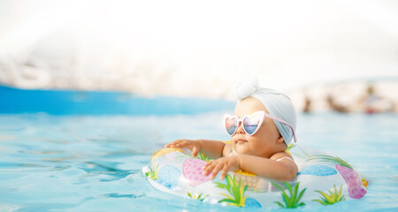 Cute funny toddler girl in colorful swimsuit and sunglasses relaxing on inflatable toy ring floating in pool have fun during summer vacation in tropical resort. Child having fun in swimming pool. 