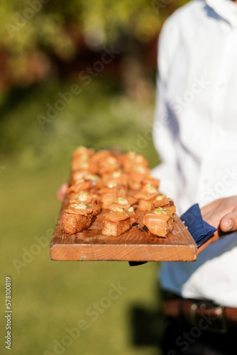Fotografi closeup of server's hands holding a wooden platter of crispy rice and salmon pas