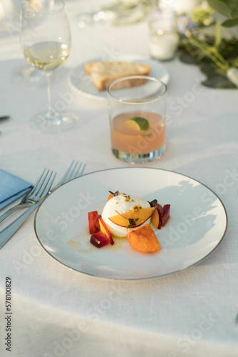 peach and burrata salad on white plate with silverware and cocktail on white tablecloth at outdoor wedding