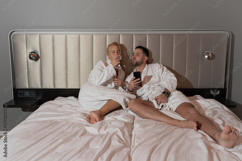Fototapeta premium A young couple is relaxing on a bed in a room drinking alcohol.
