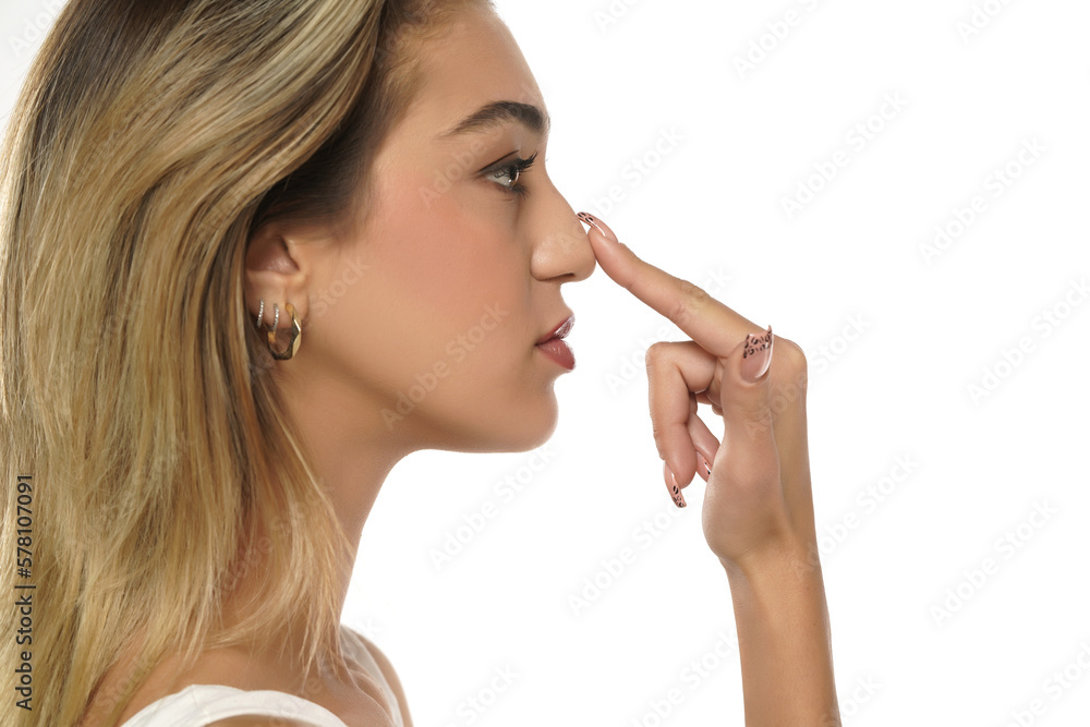 young woman touches her nose with her finger on a white background young woman touches her nose with her finger on a white background