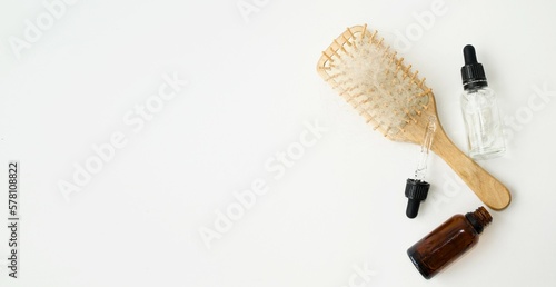 On a light background, a wooden massage comb with fallen hair, bottles with medicinal oils, biocosmetics.  The concept of hair loss, baldness, hair treatment.  Flat lay top view. photo