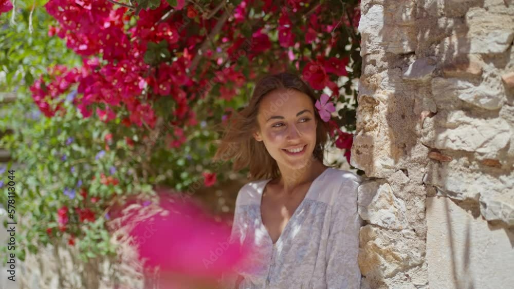 Tender beautiful lady with flower in hair wearing white dress looking to camera with smile. Concept of beauty and femininity Tender beautiful lady with flower in hair wearing white dress looking to camera with smile. Concept of beauty and femininity