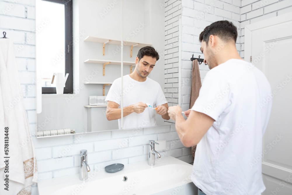 Obraz premium Handsome man brushing teeth in the bathroom. Morning routine concept